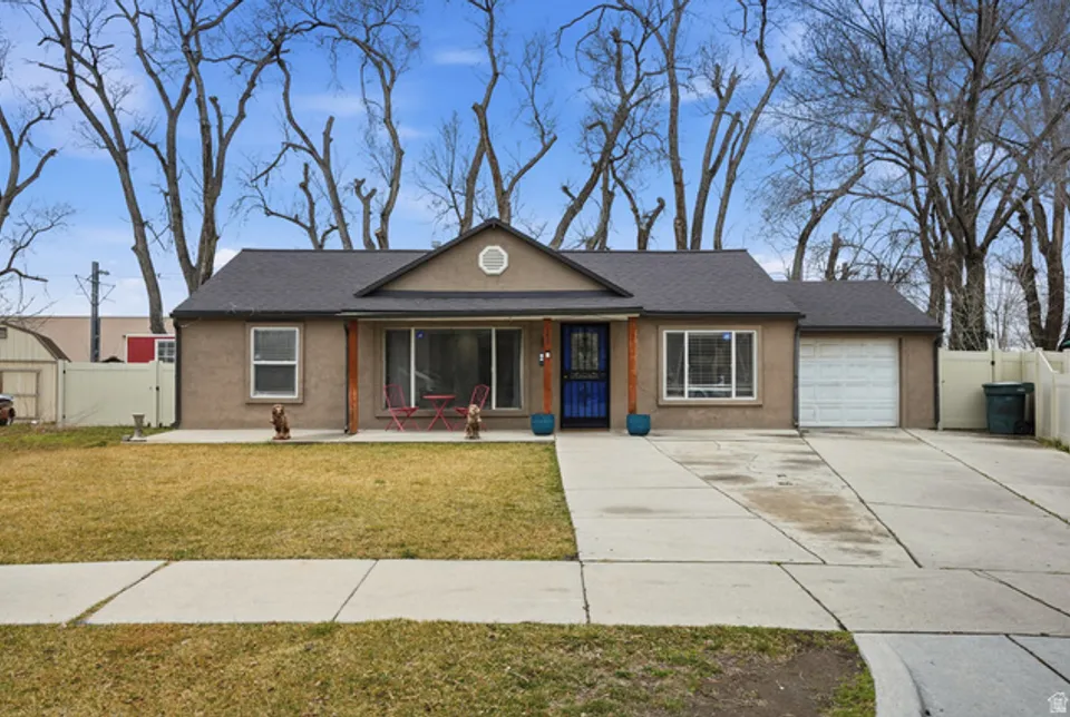 A single-story rambler with gray stucco, a covered front porch, and an attached garage on a clear winter day with bare trees behind.